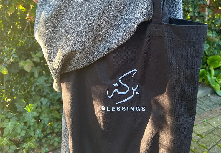 SABR Blessings tote bag in black with Arabic calligraphy and English text against a green leafy background